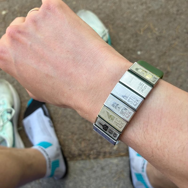 A bracelet of city-tagged 42K marathon medallions on the wrist.