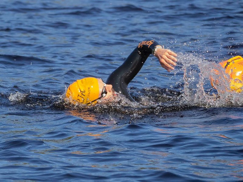 Mid-stroke in open water, orange swim cap, freestyle.